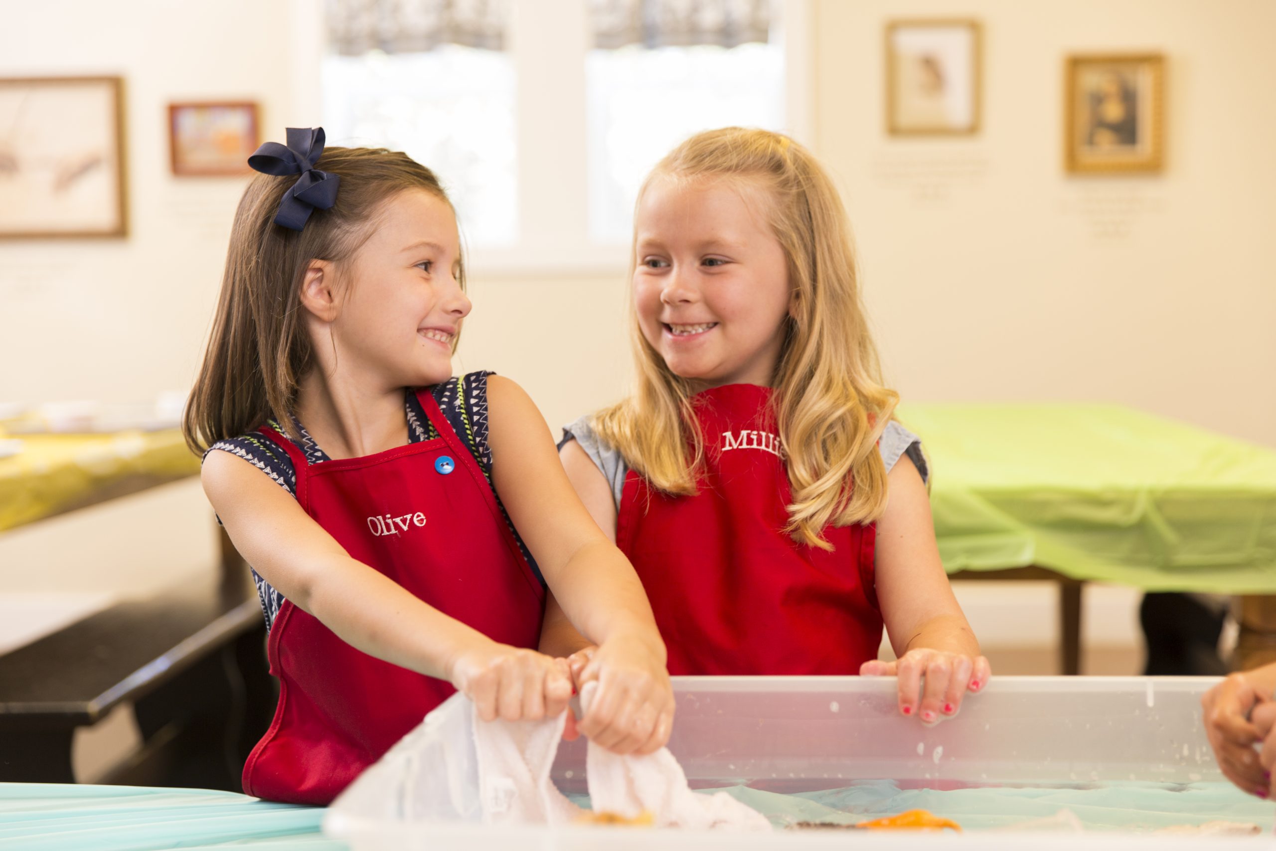 Two young girls smiling at each other and rolling dough