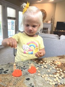 Girl practicing writing skills by placing cheerios on spaghetti noodles stuck in playdough