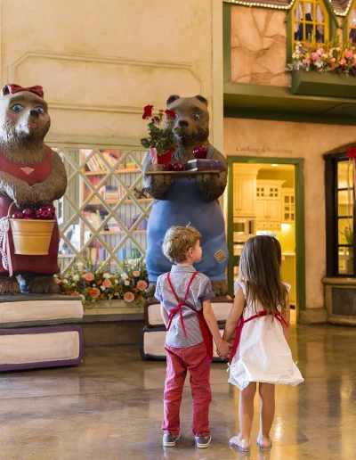 Two children on Kids Village Tour standing in front of Max the Bear and holding hands