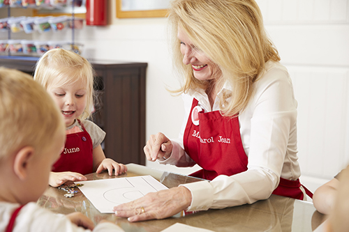 Cute female preschool student and teacher smiling at paper with letter P, getting ready to paste on puzzle pieces at Kids Village Private Pre-K in Utah County