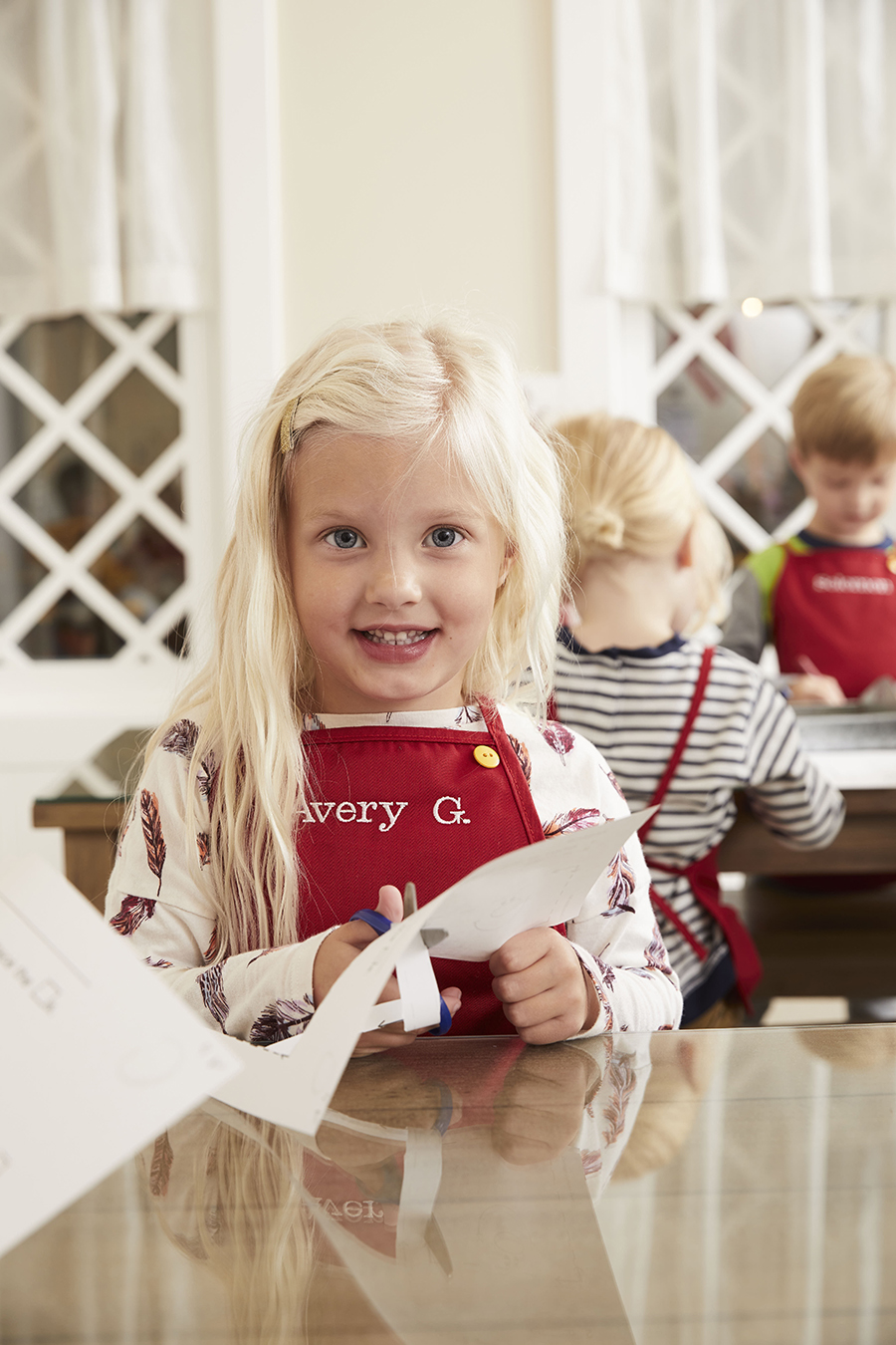 Cute little girl smiling at camera while she practices cutting paper at Kids Village, a private preschool in Orem, Utah