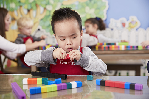 Cute 3 year old boy concentrating on putting together counting blocks at Kids Village private preschool in Orem, Utah