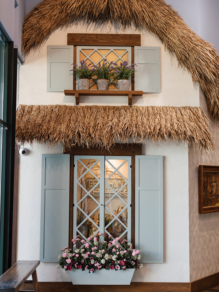 View of hallway at Kids Village, private preschool in Utah Valley, with full-sized trees and benches in the hallway and the windows of cottage store windows decorated with Valentine's Day decorations
